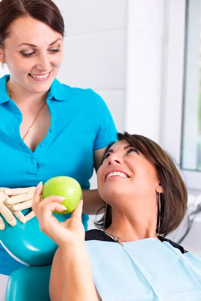 Ein zufriedener Patient an der Rezeption beim Stamotologen, überprüft den Zustand der Zähne und beißt in den grünen Jaloc. Zahnheilkonzept, gesunde Zähne, schönes Lächeln. — Stockfoto