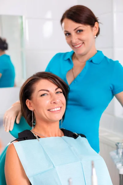 Стоматолог и ее счастливая пациентка смотрят в камеру и улыбаются. Прием у стоматолога, здоровые зубы, счастливый пациент, красивые зубы . — стоковое фото