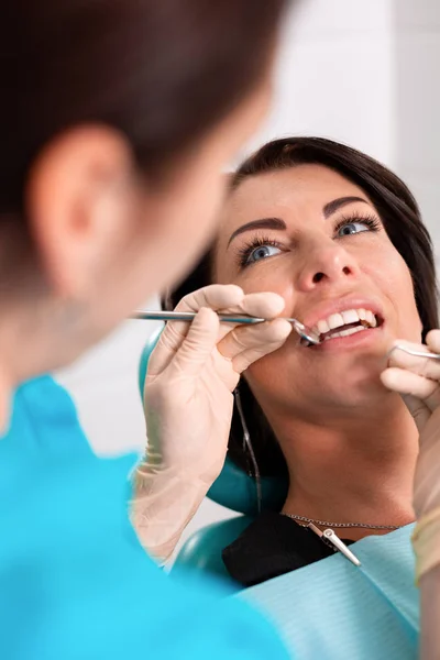 Una dentista donna esamina la cavità orale del paziente con uno strumento con uno specchio. Ritratto ravvicinato di un paziente con la bocca aperta, un medico con i guanti tiene uno specchio dentale . — Foto Stock