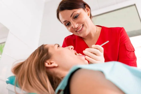 Una dentista donna esamina la cavità orale del paziente con uno strumento con uno specchio. Ritratto ravvicinato di un paziente con la bocca aperta, un medico con i guanti tiene uno specchio dentale . — Foto Stock