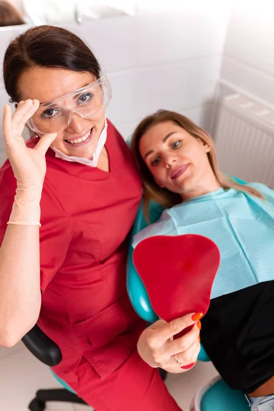 Die Zahnärztin und ihre glückliche Patientin blicken in die Kamera und lächeln. Empfang beim Zahnarzt, gesunde Zähne, glücklicher Patient, schöne Zähne. — Stockfoto