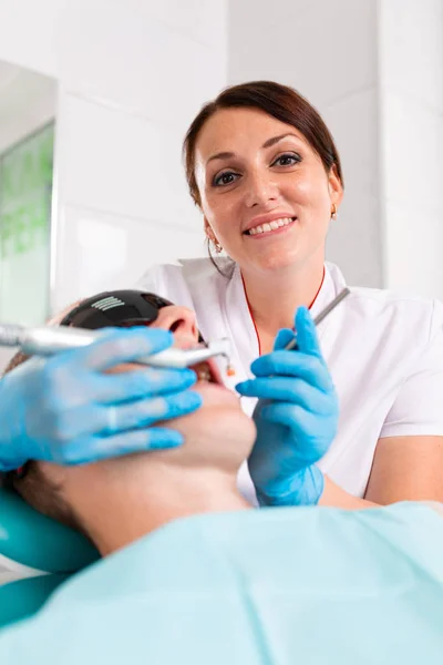 Dentystka bada jamę ustną pacjenta za pomocą narzędzia z lustrem. Portret pacjenta z otwartymi ustami, lekarz w rękawiczkach trzyma lusterko dentystyczne. — Zdjęcie stockowe