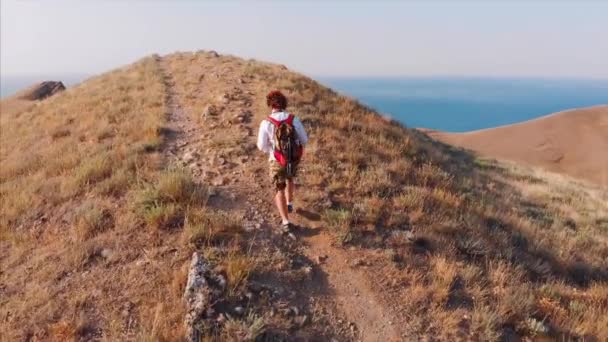 Reisender Mann mit Rucksack und Kamera, zu Fuß durch die Berge, mit einem tollen Blick auf die Berge und das Meer. Schießen von oben, das Konzept des Reisens, neue Öffnungen, Freiheit — Stockvideo