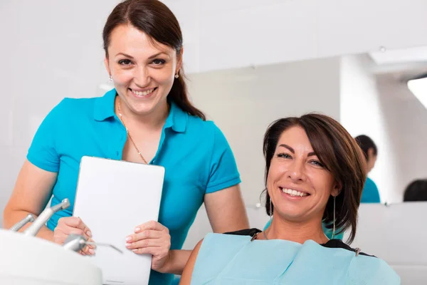 Die Zahnärztin und ihre glückliche Patientin blicken in die Kamera und lächeln. Empfang beim Zahnarzt, gesunde Zähne, glücklicher Patient, schöne Zähne. — Stockfoto