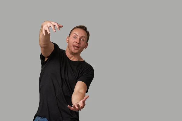 A man in a black T-shirt shows with his hands on your text or your advertisement on a gray background. Concept banner for advertising, copy space, gray background, commercial design. — Stock Photo, Image