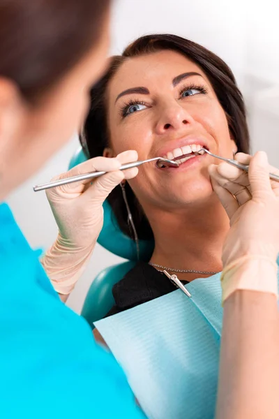 Umieszczenie szelki dentystyczne do zębów womans w gabinecie stomatologicznym. Dentysta bada pacjentkę z szelkami w gabinecie stomatologicznym. Zbliżenie młodej atrakcyjnej dziewczyny z szelkami na zębach — Zdjęcie stockowe