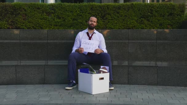 Dispensado, homem rastroenny sentado na rua, uma caixa com itens pessoais. Em torno do cartão decomposto com as palavras, demitido, desempregado, precisa de trabalho. Conceito de depressão, desmotivação — Vídeo de Stock