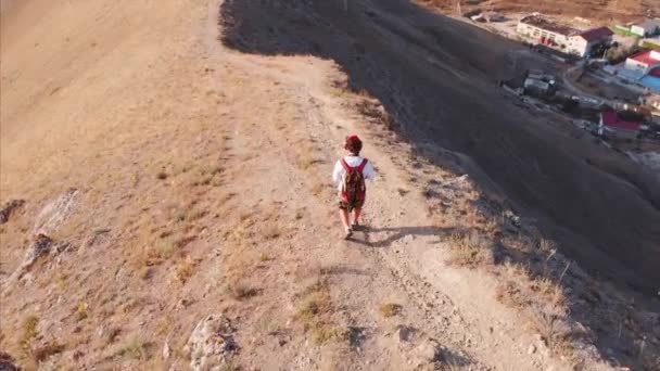 Hombre viajero con una mochila y una cámara, caminando por las montañas, con una gran vista de las montañas y el mar. Disparos desde arriba, el concepto de viaje, nuevas aperturas, libertad — Vídeo de stock