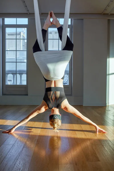 Gyönyörű lány légi jóga edző mutatja medutiruet lógó vonalak fejjel lefelé a jóga szobában. Koncepció jóga, rugalmas test, egészséges életmód, fitness. — Stock Fotó