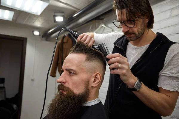 Mestre corta cabelo e barba de homens na barbearia, cabeleireiro faz penteado para um jovem — Fotografia de Stock