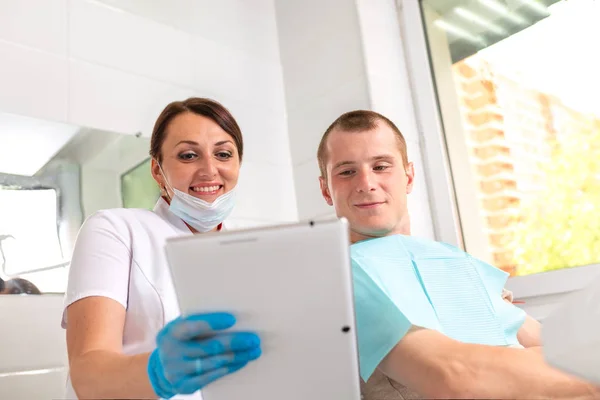 Dentista finitura restauro dei denti di successo, medico dai capelli neri, in maschera verde, dando a specchio paziente felice, bella donna dai capelli lunghi guardando denti bianchi incontaminati con grande piacere — Foto Stock