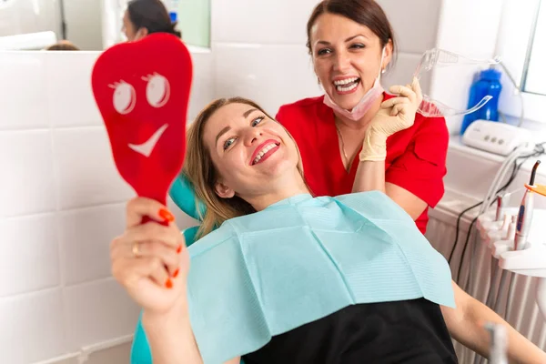 Die Zahnärztin und ihre glückliche Patientin blicken in die Kamera und lächeln. Empfang beim Zahnarzt, gesunde Zähne, glücklicher Patient, schöne Zähne. — Stockfoto