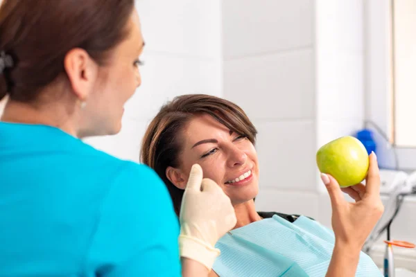 Un paziente felice alla reception presso lo stamatologo, controlla la salute dei denti, morde mele verdi. Concetto di odontoiatria, denti sani, bel sorriso . — Foto Stock