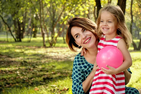 Mom hugs a little girl holding a balloon in the park. Happy family, mom daughter.