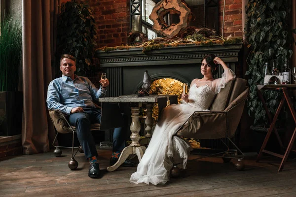 Hermosa pareja de boda posando en cámara en un restaurante. Los recién casados se sientan junto a la chimenea y se toman de la mano, el concepto es una nueva familia, una hermosa boda . — Foto de Stock