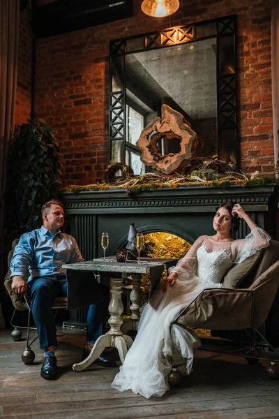 Hermosa pareja de boda posando en cámara en un restaurante. Los recién casados se sientan junto a la chimenea y se toman de la mano, el concepto es una nueva familia, una hermosa boda . — Foto de Stock