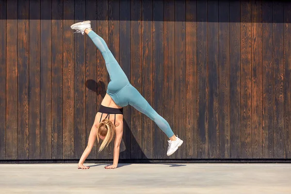 Красивая атлетичная юная гимнастка в спортивной одежде, тренирующаяся, элемент гимнастики, делающая сплит. деревянный и бетонный фон. Спортивная мотивация, копировальное пространство, баннер для рекламы . — стоковое фото