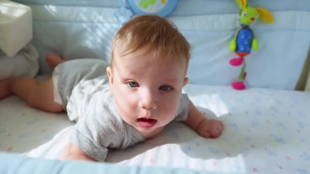 A kisbaba a kiságy nevet, és megpróbálja feltérképezni. Boldog gyermekkori, gyerekes öröm, az első lépések az életben. — Stock videók
