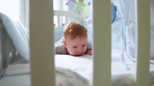 Primer plano de un niño pequeño en una cuna riéndose vista lateral a través del enrejado de una cuna. Feliz infancia, alegría infantil, los primeros pasos de la vida . — Vídeos de Stock