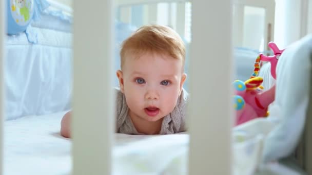Close-up de uma criança em um berço rindo vista lateral através da treliça de um berço. Infância feliz, alegria infantil, os primeiros passos na vida . — Vídeo de Stock