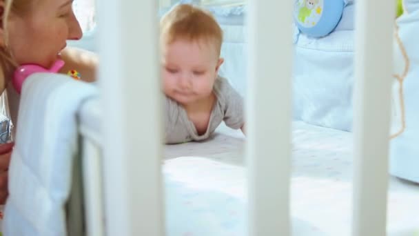 Primo piano mamma gioca con un bambino nella culla ridendo vista laterale attraverso il traliccio della culla. Infanzia felice, gioia infantile, i primi passi nella vita . — Video Stock