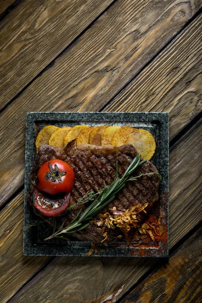 Filete a la parrilla con cuchillo y tenedor tallado en pizarra de piedra negra. Filete en una piedra de mármol caliente. Copiar el espacio, fondo oscuro, comida foto de moda . — Foto de Stock