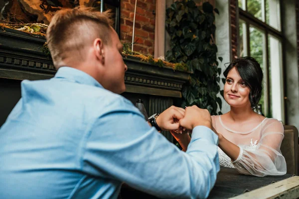 美丽的婚礼情侣在餐厅里摆出相机的样子。新婚夫妇坐在壁炉旁,手牵手,理念是一个新的家庭,一个美丽的婚礼. — 图库照片
