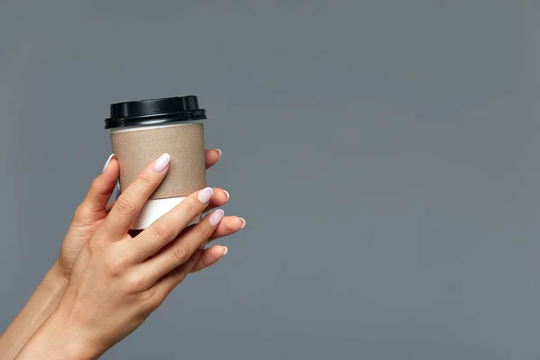 Красивая женская рука предлагает горячий напиток, чай или кофе в одноразовом натуральном стекле на светло-сером фоне. КОНЦЕПТ начало дня с чашечки кофе — стоковое фото