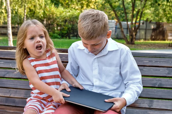 Koncepció Gadget küzdelem. Egy lány vesz egy laptopot egy fiú egy padon egy városi parkban — Stock Fotó