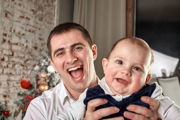 Atento padre cariñoso jugando con su hijo pequeño en trineo de madera blanca alrededor de un árbol de Navidad con cajas de regalo de año nuevo —  Fotos de Stock