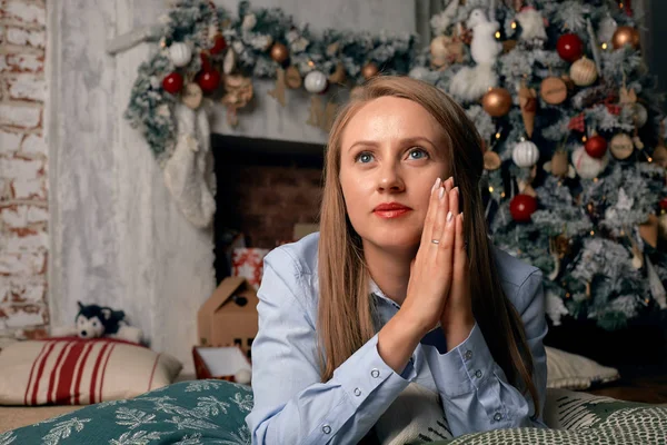 Hermosa mujer joven en la víspera de Navidad, se encuentra frente a una chimenea con un árbol de Navidad y la decoración de Año Nuevo y sueños. Concepto deseos de Navidad se hacen realidad. Esperando un milagro para el nuevo — Foto de Stock