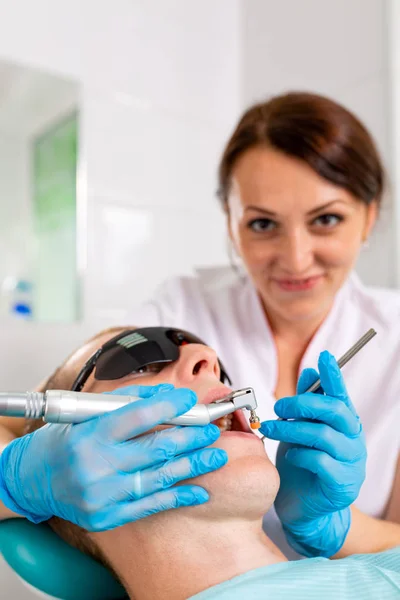 Jovem visitando o consultório odontológico. Mãos de dentista em luvas de proteção usando ultra-som para limpar os dentes dos pacientes. Fechar a boca aberta . — Fotografia de Stock