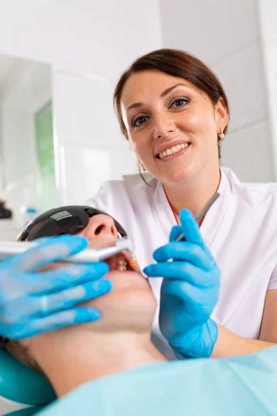 Jonge man een bezoek aan de tandheelkundige kantoor. Tandarts handen in beschermende handschoenen met behulp van echografie te reinigen patiënten tanden. Close-up van open mond. — Stockfoto