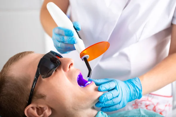 Zahnarzt fixiert Dichtung UV-Lampe. Zahnarzt macht den Prozess der Behandlung von jungen Mann. — Stockfoto
