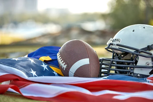 Concepto de fútbol americano. Equipo de fútbol americano, casco, bola de primer plano en el fondo de la bandera estadounidense. Patriotismo . — Foto de Stock