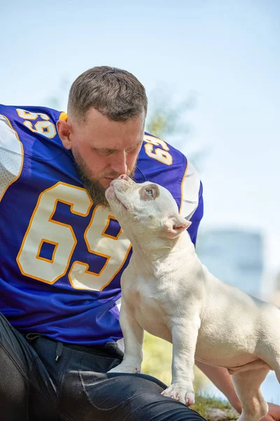 American football player with a dog posing on camera in a park. Copy space, sports banner. Concept american football, sport for the protection of animals.