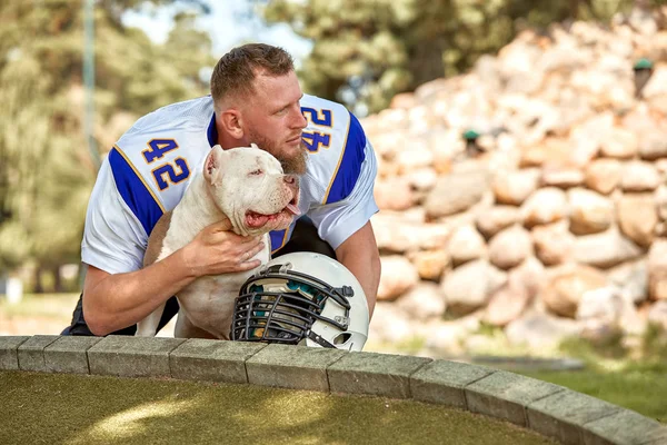 American football player with a dog posing on camera in a park. Copy space, sports banner. Concept american football, sport for the protection of animals.