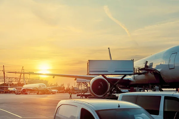 Modern passenger airplane parked to terminal building gate at airside apron of airport with close up airplane parts jet engine wing windows gear tow tractor noon sun view