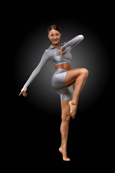 Sexy brunette girl with a slim figure in leggings posing in studio on a black background — Stock Photo, Image