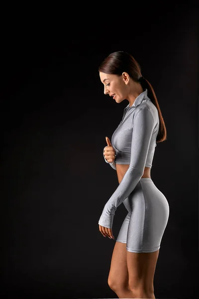 Sexy brunette girl with a slim figure in leggings posing in studio on a black background — Stock Photo, Image