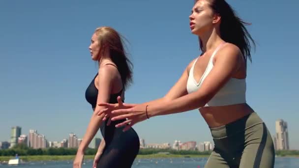 Två kvinnor gör övningarna sport på stranden av floden i staden. Övningar utomhus. — Stockvideo