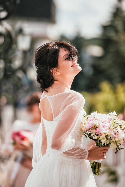 Young brunette bride in a white dress with bouquet. Closeup portrait of a woman outdoor