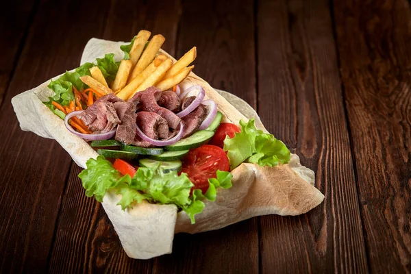 Meat salad with beef and fresh vegetables and lettuce in a plate-baked pita bread. Copy space, wooden background. — Stock Photo, Image