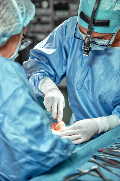 在手术室工作的一组外科医生。 几个外科医生正在一个真正的手术室里做手术. 蓝光，白色手套垂直射击. — 图库照片