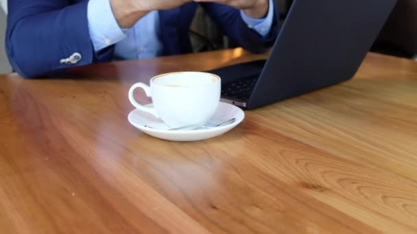 Jonge Europese zakenman zit aan een tafel in een café en typt op een laptop terwijl hij aan een koffiepauze werkt. — Stockvideo