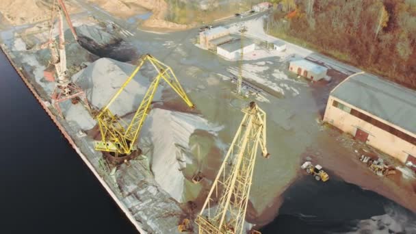 Havenkranen op de oever van de rivier produceren zand. Bakboordkranen met een emmer op de rivieroever. Winning van rivierzand. Havenkranen onttrekken rivierzand, productie. Zonsondergang. Schip. — Stockvideo