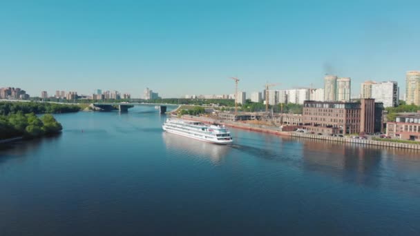 Beautiful landscape with a white ship sailing along the river near steep banks covered with green forest. Stock footage. White vessel moving against grey cloudy sky, river transportation concept. — Stock Video