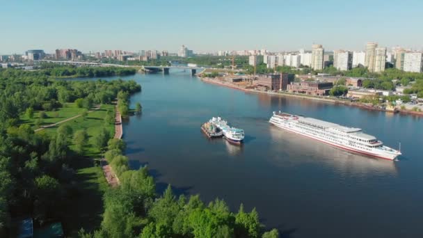Beautiful landscape with a white ship sailing along the river near steep banks covered with green forest. Stock footage. White vessel moving against grey cloudy sky, river transportation concept. — Stock Video