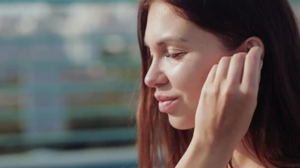 Hermosa chica inserta auriculares en los oídos, buen humor, primer plano, al aire libre — Vídeos de Stock