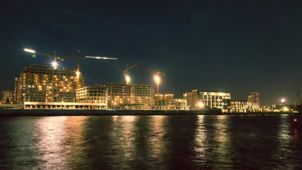 Временные лаборатории строительства многоэтажных зданий на набережной реки в городе. Ночная стрельба, светящиеся грузовые краны, ночной город . — стоковое видео